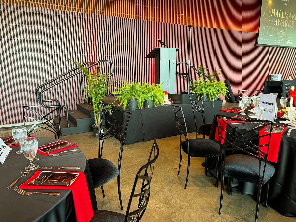 wide shot of a formal corporate award ceremony stage setup inside a hotel ballroom with pipe and drape backdrop, podium stage left, and banquet table seating in the foreground